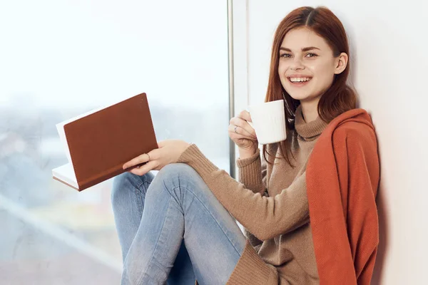 Mujer con un libro cerca de la ventana con una taza de café — Foto de Stock