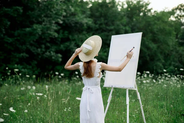 Жінка в білій сукні в полі з квітами малює картину — стокове фото