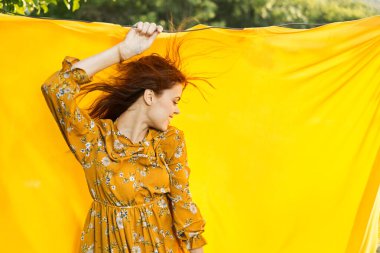 Sarı elbiseli gülümseyen kadın doğaya sarılık pozu veriyor.