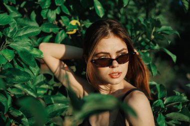 Güneş gözlüklü ve yeşil yapraklı neşeli moda kadın Rus yazı