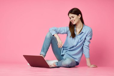 Dizüstü bilgisayarı olan bir kadın internet iletişiminde pembe arka planda oturuyor.
