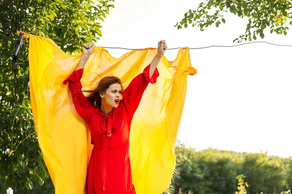 woman in a red dress with hands raised up yellow fabric nature