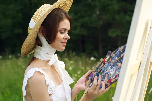 Όμορφη γυναίκα στο καπέλο καλλιτέχνης ζωγραφίζει μια εικόνα για το χρώμα της φύσης — Φωτογραφία Αρχείου