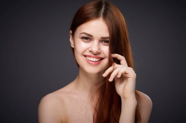 Güzel, kızıl saçlı, çıplak omuzlu, siyah arka plan pozu veren bir kadın.