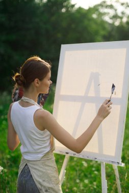 Kadın ressam açık havada palet boyayıp manzara resmi yapıyor.