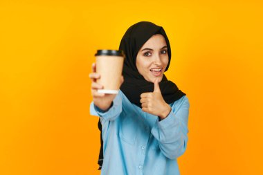 Siyah tesettürlü kadın. Yüz stüdyosunun yanında elinde bir bardak kahve.