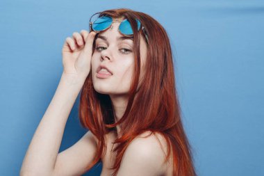 Şık kızıl saçlı, mavi gözlüklü, çıplak omuzlu bir kadın.