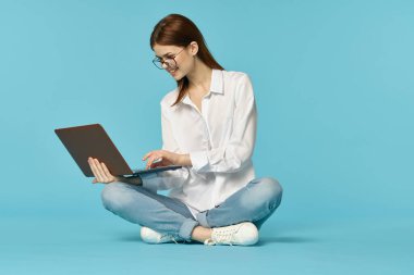 Dizüstü bilgisayarı olan kadın yerde oturuyor ve mavi arka planda öğrenci teknolojisi öğreniyor.