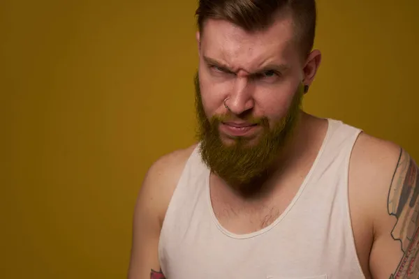 A bearded man with a serious expression in a white t-shirt with tattoos on his arms — Stock Photo, Image