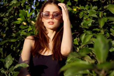 Güneş gözlüğü takan çekici kadın yaz mevsiminde tropik doğaya poz veriyor.