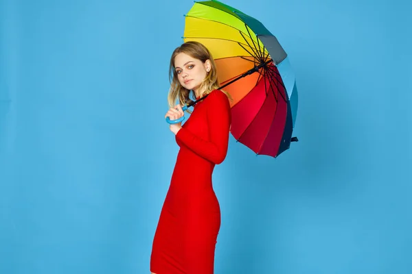 Vrouw in rode jurk veelkleurige paraplu blauwe achtergrond — Stockfoto