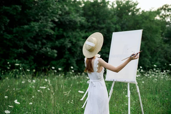 Kobieta w białej sukience na polu z kwiatami maluje obraz — Zdjęcie stockowe