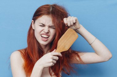 Güzel bir kadın yaramaz saçlarını mavi arka planda tarıyor