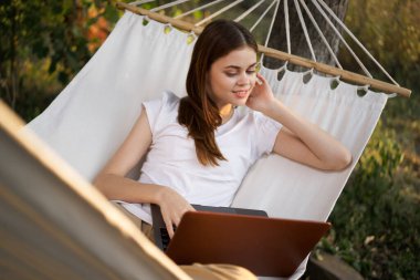 Neşeli kadın bir hamakta dizüstü bilgisayarla yatıyor.