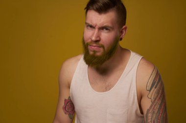 Beyaz tişörtlü, kollarında dövmeleri olan sakallı bir adam.