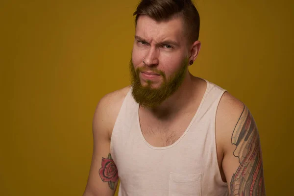 Un hombre barbudo con una expresión seria en una camiseta blanca con tatuajes en los brazos —  Fotos de Stock