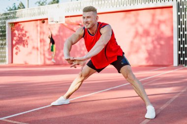 Spor salonunda spor yapan kırmızı tişörtlü bir adam egzersiz yapıyor.