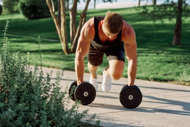 Dambılı atletik adam dışarıda motivasyon egzersizi yapıyor.