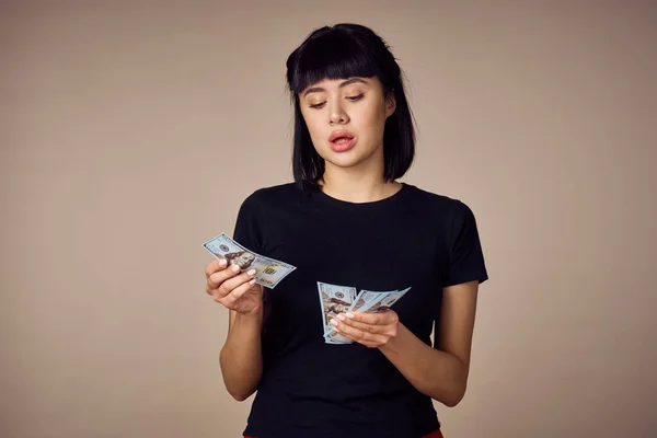 Γυναίκα σε ένα μαύρο t-shirt ένα μάτσο χρήματα δολάρια πληρωμή μπεζ φόντο — Φωτογραφία Αρχείου