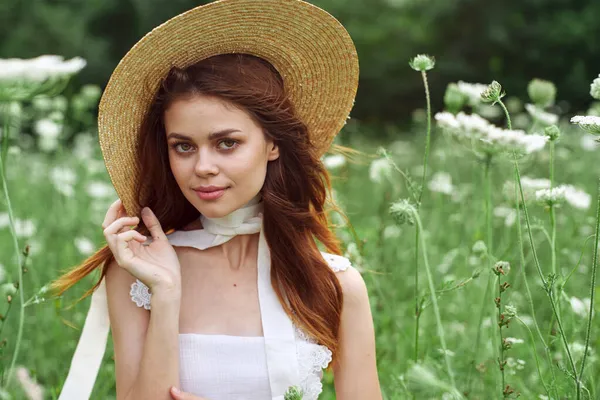 Vacker kvinna i vit klänning och hatt poserar blommor natur — Stockfoto