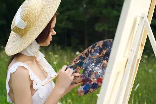 Mooie vrouw in hoed kunstenaar schildert een beeld op de natuur verf — Stockfoto