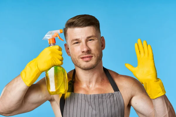 Man in apron with pumped up body rubber gloves cleaning blue background — Stock Photo, Image