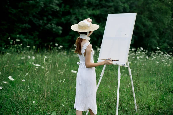 Женщина в белом платье в поле с цветами рисует картину — стоковое фото