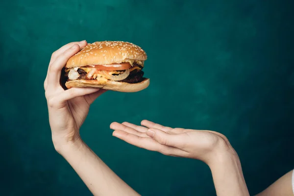 Hamburger in handen close-up fast food groene achtergrond — Stockfoto