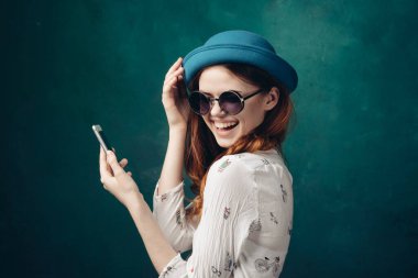 Mavi şapkalı şık bir kadın. Elinde telefon, iletişim teknolojisi var.