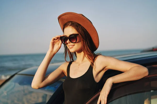 Fröhliche Frau mit Sonnenbrille und Hut auf dem Meer in der Nähe des Autos — Stockfoto