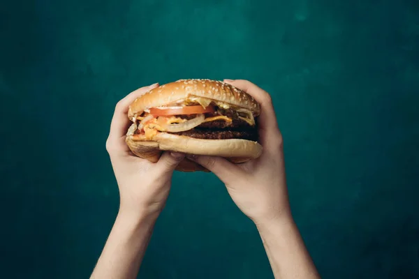 Hamburger in handen close-up fast food groene achtergrond — Stockfoto