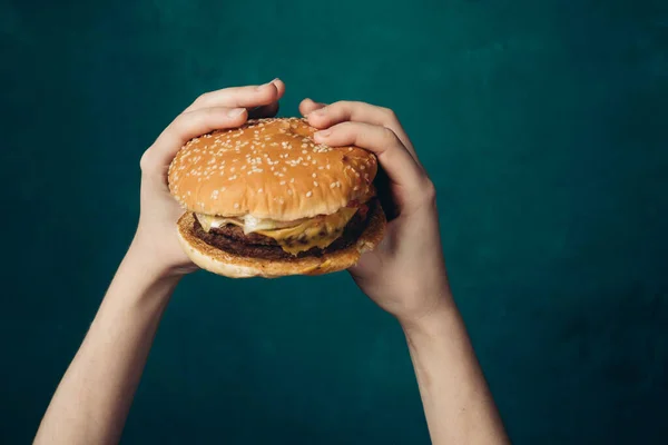 Hamburger in handen close-up fast food groene achtergrond — Stockfoto