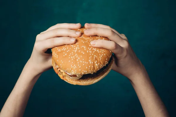 Hamburger in handen close-up fast food groene achtergrond — Stockfoto