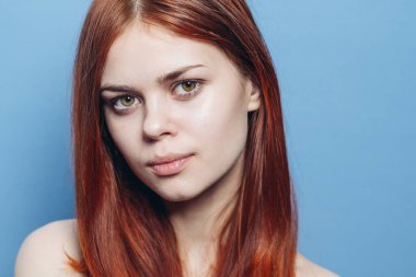 Çıplak omuzlu çekici bir kadın. Kızıl, yakın plan, mavi arka plan.