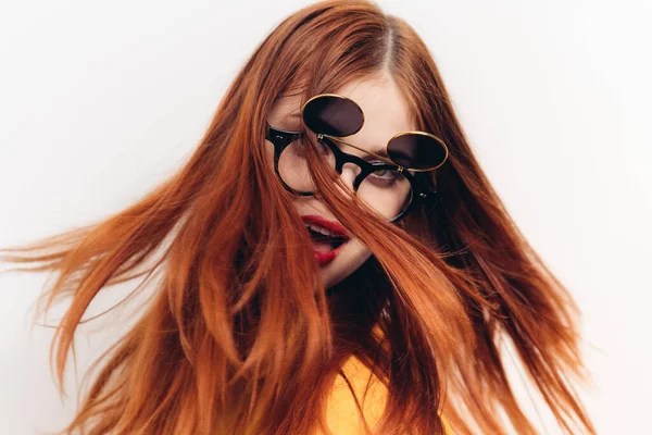 Κοκκινομάλλα γυναίκα φορώντας γυαλιά ηλίου ποζάροντας φως μόδας φόντο — Φωτογραφία Αρχείου