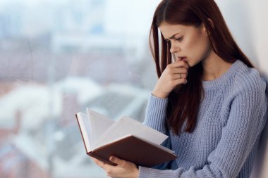 Kadın pencerenin yanında kitap okuyor, bir bardak içkiyle dinleniyor.