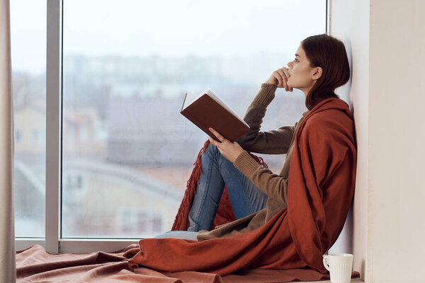 woman near the window with a plaid cup of hot drink rest