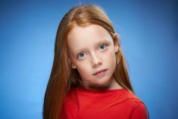 Cute red-haired girl in red t-shirt emotions blue background — Stock Photo, Image