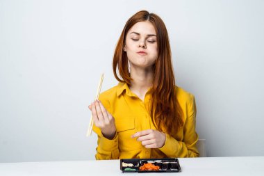 Sarı gömlekli bir kadın masaya oturur ve suşi yer.