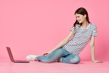 Dizüstü bilgisayar alışverişi yapan pembe arka planda oturan bir kadın.