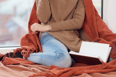 Pencere kenarında bir bardak içkiyle kitap okuyan bir kadın.