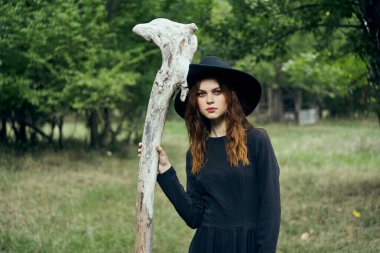 Siyah cadı kostümlü kadın orman doğasında poz veriyor.