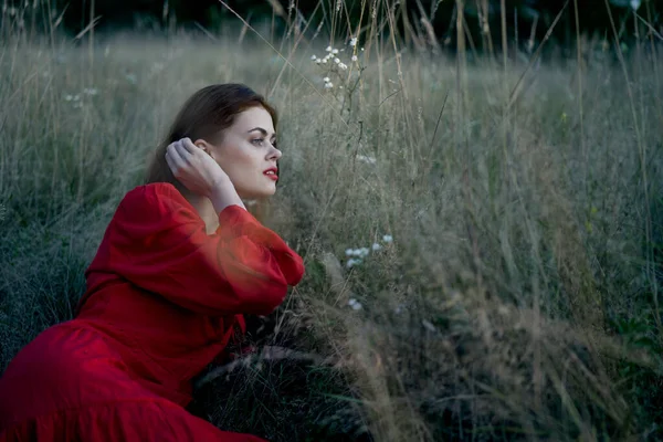 Tarladaki kadın kırmızı elbiseli çimenlerin üzerinde yatıyor. — Stok fotoğraf