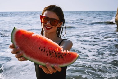 Ellerinde karpuz olan siyah mayo giymiş güzel bir kadın.