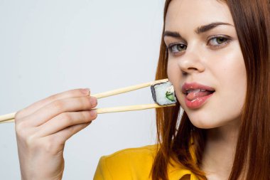 Japon yemek çubuklarıyla suşi yiyen kadın arka planda ışık yayıyor.