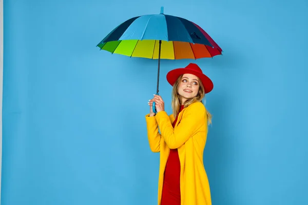 身穿黄色外套、头戴彩色雨伞、身披蓝色背景的女人 — 图库照片