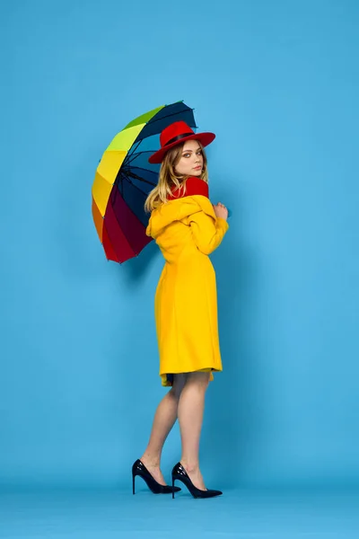 黄色のコートを着た女性多色の傘ポーズ青の背景 — ストック写真