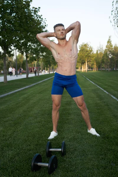 Parkın ortasında dambılı kaslı bir adam.