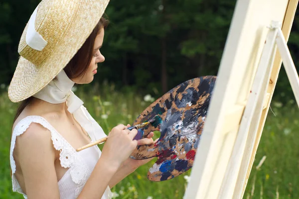 Mooie vrouw in hoed kunstenaar schildert een beeld op de natuur verf — Stockfoto