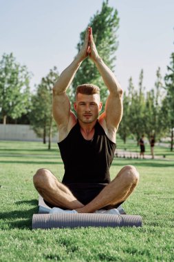 Sportif adam parkta çimlerde oturuyor.